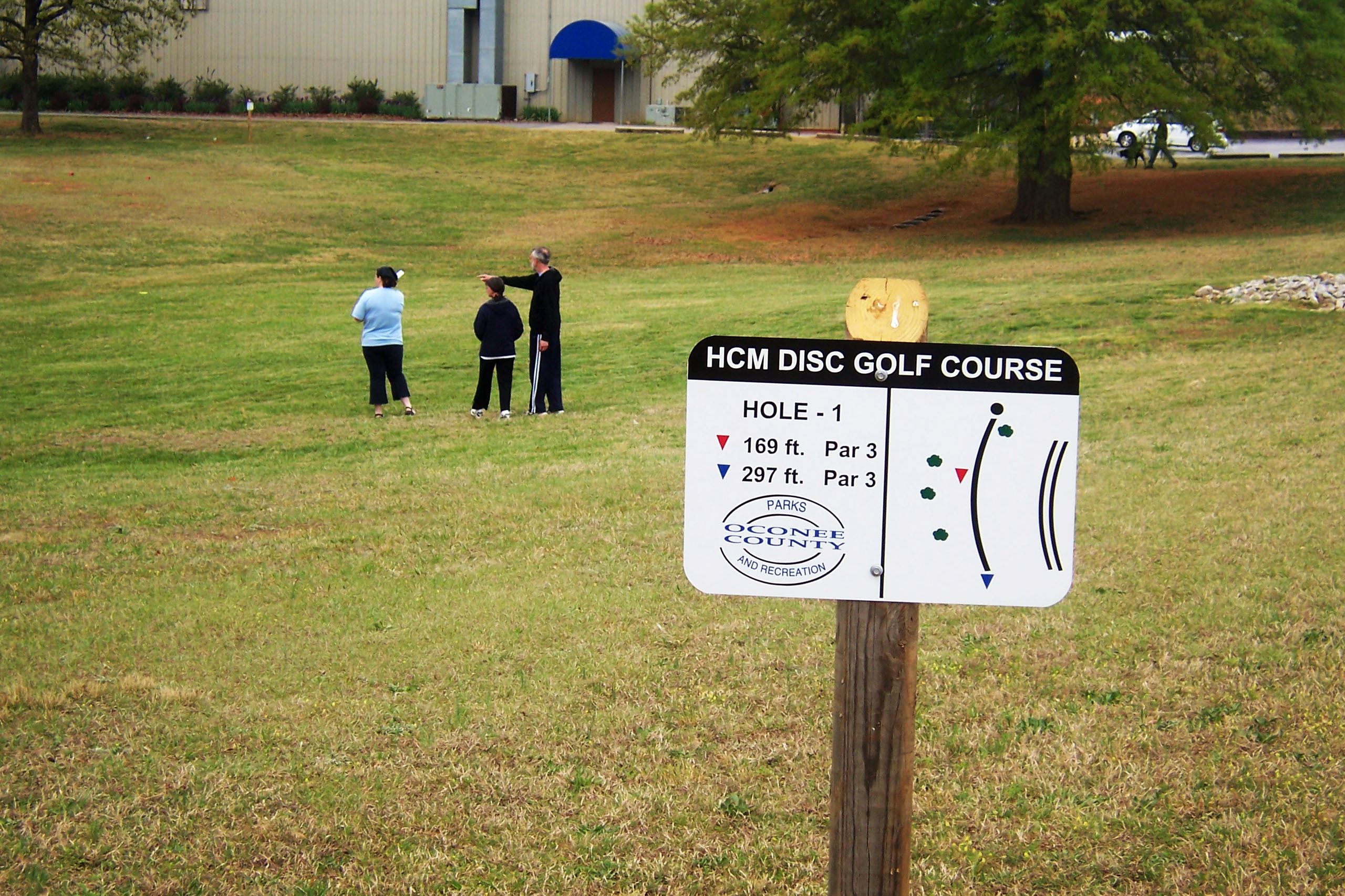 Disc Golf Course Sign Hole 1 with family playing disc golf in background